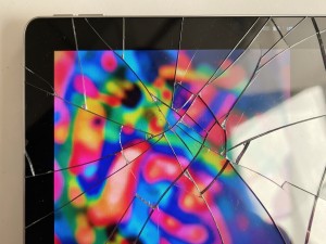 Section of a tablet computer screen showing cracked glass overlaying a colorful digital pattern, photo