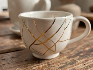 Close-up macro of a cracked ceramic teacup with gold kintsugi repair lines on a rustic wooden table