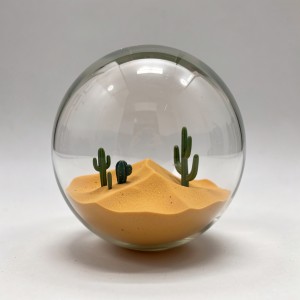 Transparent glass sphere containing a miniature desert landscape with dunes and cacti