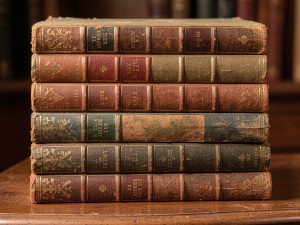 Stack of old hardcover books with cloth bindings and gold leaf titles