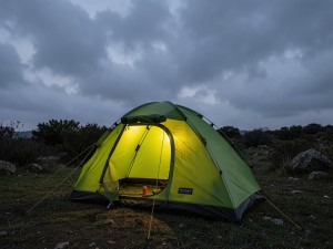 Lighted green camping tent under cloudy sky, photo