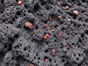 Dark volcanic rock surface with scattered dried lava droplets and rough vesicles, photo